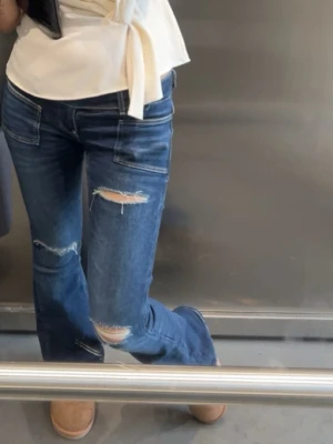 Blå bootcut jeans med slitningar - Säljer de snygga populära jeansen ifrån gina 14+ i storlek Xs. Jag är 164 och de är bra i längden på mig. blå bootcut jeans med slitna detaljer på knäna och låret. Jeansen har låg midja och fickor fram och bak. 