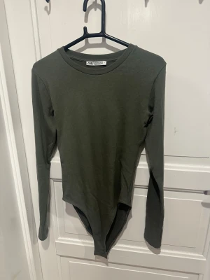 Mörkgrön långärmad bodysuit från Zara - Mörkgrön bodysuit från Zara med lång ärm och rund halsringning. Tillverkad i mjuk bomullsmix. 