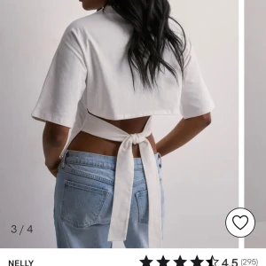 Vit kortärmad topp med knyt från Nelly - Säljer en stilren vit topp från Nelly med korta ärmar och en unik knytning i ryggen. Toppen har en croppad passform som ger en modern look. Perfekt för att skapa en trendig outfit.