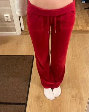 Röda Juicy Couture byxor - Röda mjukisbyxor från Juicy Couture med snörning i midjan och fickor både fram och bak. Byxorna har en loose passform och bred resår i midjan. Snygga detaljer med silverfärgade metalldelar på snöret och knappar på bakfickorna. Inga defekter. Nypris 1299kr.