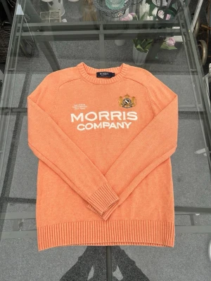 🧡 Morris Company stickad tröja – flicka | Strl S - Fin och klassisk stickad tröja från Morris Company i en mjuk orange/korallfärg. Tröjan har rund hals, ribbade kanter och en stilren design med broderad Morris-logga framtill. Tillverkad i 100 % bomull, vilket gör den skön att bära och passar perfekt till både skola och fritid.  En tidlös tröja i preppy och klassisk stil som är lätt att matcha med jeans, kjol eller leggings. Perfekt året runt och funkar både till vardag och finare tillfällen.  🔸 Märke: Morris Company 🔸 Storlek: S 🔸 Färg: Orange