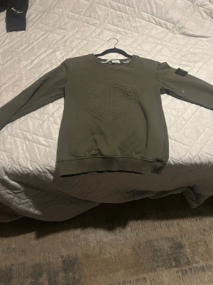 Stone Island grön sweatshirt slim fit - Snygg grön sweatshirt från Stone Island i slim fit med broderad logga på bröstet och klassisk patch på ärmen. Tröjan har rund hals, långa ärmar och ribbade muddar. Perfekt för dig som gillar streetwear och vill ha en clean look. Barn storlek 