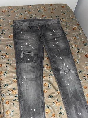 Grå Dsquared2 jeans med färgstänk - Snygga grå jeans från Dsquared2 med coola vita färgstänk och slitna detaljer på benen. Modellen har klassisk femficksdesign, normal passform och raka ben. Jeansen är tillverkade i bomull och har en urban vibe som sticker ut.