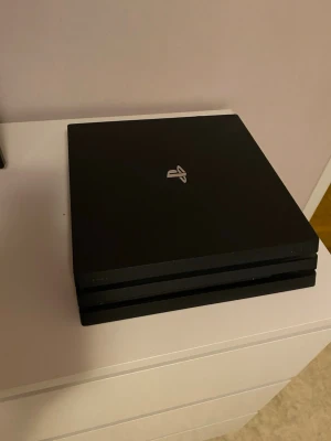 PlayStation 4 Pro - Sony PlayStation 4 Pro i svart, i fint skick. Konsolen har tre lager och flera anslutningar på baksidan, inklusive HDMI, USB och Ethernet. Inga synliga repor eller skador. Perfekt för gaming i hög upplösning och med extra prestanda.