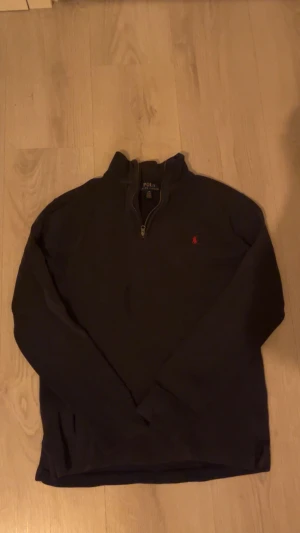 Marinblå half zip tröja från Polo Ralph Lauren - Marinblå långärmad tröja från Polo Ralph Lauren med half zip och ståkrage. Klassisk röd logobrodering på bröstet. Tröjan är i bomull och har en clean, normal passform som funkar till många olika stilar.