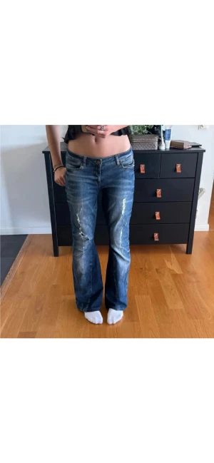 Blå bootcut jeans från Noisy May - Snygga blå jeans från Noisy May med bootcut passform och låg midja. Jeansen har slitna detaljer och klassisk femficksdesign. Materialet är jeans med en skön stretch och de har dragkedja och knapp framtill.