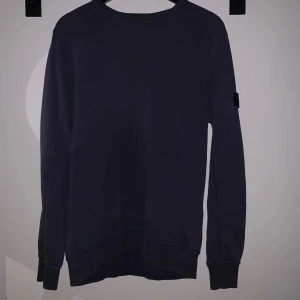 Mörkblå sweatshirt från Stone Island  - Säljer en mörkblå sweatshirt från Stone Island Junior. Tröjan har rund halsringning, långa ärmar och klassisk patch på ena ärmen. Perfekt för en stilren och avslappnad look.