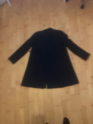 Svart klassisk kappa med knappar - Snygg svart kappa med rak passform och knappar framtill. Jackan har lång ärm och slits baktill för extra rörelsefrihet. Fodrad insida som ger en skön känsla och stilren look. Perfekt för dig som gillar minimalistisk och tidlös design.