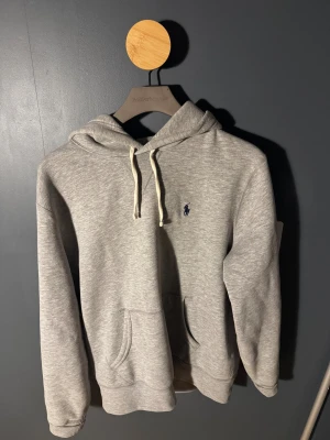 Ralph Lauren Polo Hoodie - Hej! 👋 Säljer en äkta Ralph Lauren Polo hoodie i klassisk grå färg. En tidlös hoodie i mjukt, tjockt och bekvämt material med den ikoniska broderade Polo-loggan på bröstet. Passformen är riktigt bra och färgen är lätt att matcha till allt. Hoodien är i väldigt fint skick och väl omhändertagen. Nypris och marknadsvärde ligger betydligt högre än mitt pris. Pris: 999 kr – ett riktigt bra kap för premiumkvalitet. Först till kvarn!