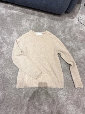 Beige stickad tröja från A Days March - Snygg beige stickad tröja från A Days March med rund hals och ribbade muddar vid ärmslut och nederkant. Perfekt för dig som gillar stilrena och enkla plagg. Materialet är mjukt och skönt, passar till många olika outfits.