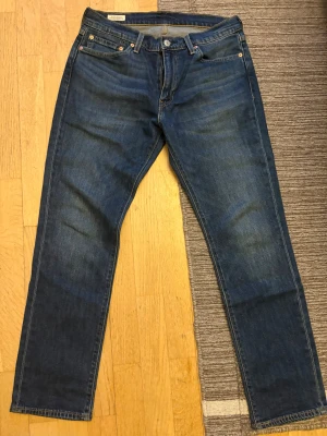 Levi's 511 blå jeans W32 L30 - Säljer ett par klassiska Levi's 511 jeans i mörkblå denim. Modellen är slim fit med raka ben och fem fickor. Snygga kontrastsömmar och ikonisk läderpatch bak i midjan. Perfekta för dig som gillar en tidlös och clean look.