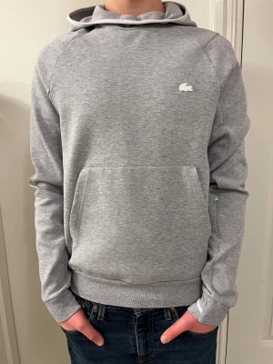 Grå hoddie från Lacoste. - En riktig sjyst grå hoddie från Lacoste med vit märke där fram och grönt där bak. 