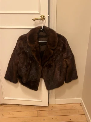 Mörkbrun pälsjacka med krage - Säljer en snygg mörkbrun pälsjacka med bred krage och rak passform. Jackan är fodrad och har en klassisk look som ger en lyxig känsla. Perfekt för dig som vill sticka ut och hålla dig varm under kallare dagar.