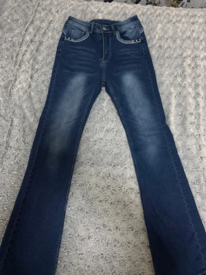 2st Högmidjade utsvängda jeans  - Säljer ett par blå jeans med coola stjärndetaljer på fickorna och kontrastsömmar. Jeansen har en klassisk femficksdesign, normal passform och raka ben. Materialet är jeans med snygga slitningar och tvättade effekter. Perfekt för dig som gillar unika detaljer! Dom är helt nya båda är högmidjade och i jättebra skick. Båda är i storlek S och säljer dom tillsammans för 200kr