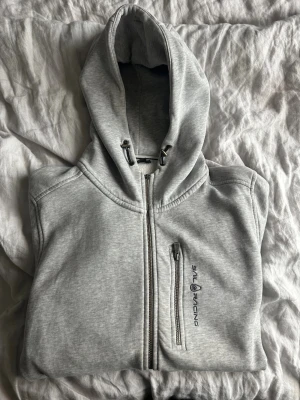 Ljusgrå zip hoodie Sail Racing, L - Ljusgrå zip-hoodie från sail racing i bra skick! Ett minus då dragkjed ”knappen” har lossnat men funkar bra att använda ändå! Mycket stilren och fin tröja! Storlek L!