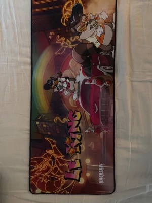 Hacksaw Gaming Musmatta - ”Le King” - Färgglad och stor musmatta med motiv från Le King, prydd med tecknade katter, retrobil och neonfärger. Perfekt för gaming eller skrivbordet. Tillverkad i mjukt tyg med gummibotten för bra grepp.