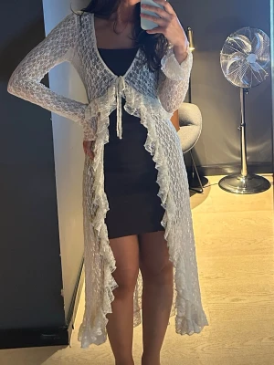 Vit lång kaftan med volang - Superfin lång vit kofta med volangkant och knyt framtill. Klänningen är genomskinlig och har långa ärmar, använd endast en gång. 