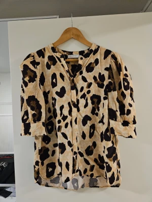 Leopardmönstrad blus - Trendig blus med leopardmönster i beige, svart och bruna toner från Object. Blusen har trekvartsärm med lätt puff och knäppning framtill. Perfekt för dig som vill sticka ut med ett djurmönstrat plagg i garderoben.