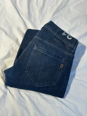 Mörkblå dondup George jeans - Säljer ett par mörkblå dondup George klassisk femficksmodell. Jeansen har en smal passform och är tillverkade i ett slitstarkt denimtyg av bomull. Perfekta för dig som gillar stilrena och tidlösa jeans.