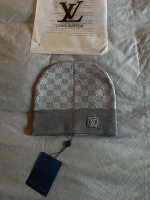 LVmössa - Snygg grå mössa från  med klassiskt rutmönster och vikbar kant. Mössan har en diskret logga framtill och är tillverkad i mjukt stickat material som känns lyxigt och bekvämt. Perfekt accessoar för dig som gillar exklusiv streetstyle.