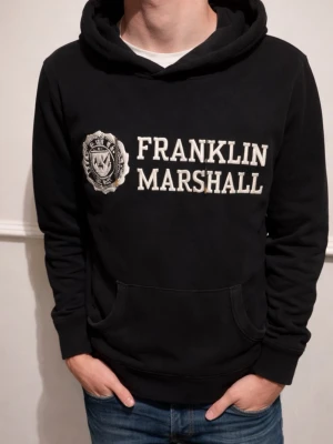Sällsynt Svart hoodie från Franklin & Marshall - Säljer en svart hoodie från Franklin & Marshall med stor vit logga och emblem på bröstet. Klassisk känguruficka framtill och huva. Perfekt för en avslappnad och sportig stil. Mjuk bomullskänsla och ribbade muddar vid ärmar och midja.