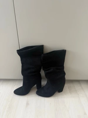 Svarta mockastövlar med klack - Snygga svarta stövlar i mocka med rund tå och låg klack. Stövlarna har en slouchy design som ger en avslappnad men trendig look. Perfekta att styla till både jeans och kjol.