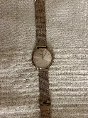 Emporio Armani mesh klocka - Stilren klocka från Emporio Armani med roseguldfärgat mesh armband i rostfritt stål. Urtavlan är ljus med diskreta stenar som timmarkeringar och logga upptill. Slutsåld på Zalando, där pris ligger på 3000kr. 