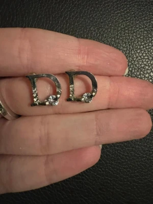 Örhängen med bokstaven D och sten - Snygga örhängen i form av bokstaven D i silverfärgad metall med stenar i. Helt nya!