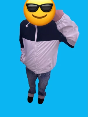 Svartvit vindjacka med huva - Snygg svartvit vindjacka med huva och dragsko. Jackan har dragkedja framtill, två fickor och elastiska muddar vid ärmsluten. Perfekt för blåsiga dagar och enkel att matcha med jeans eller sneakers.