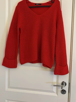 Röd stickad tröja från Gina Tricot - Snygg röd stickad tröja från Gina Tricot med v-ringning och långa ärmar. Tröjan har breda muddar vid ärmsluten och är gjord i ett grovstickat material. Perfekt för att hålla värmen och ge en pop av färg till din outfit.