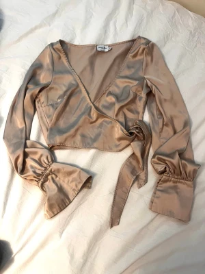 Champagnefärgad omlottopp i satin - Snygg champagnefärgad omlottopp i satin med långa ärmar och knyt i midjan. Skriv om ni har frågor💕