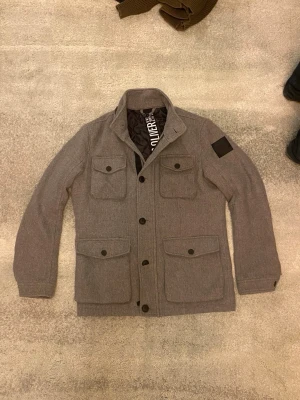 Grå fieldjacka från s.Oliver  - Säljer en riktigt snygg och stilren grå overshirt från s.oliver med fyra stora fickor framtill och knappar längs hela framsidan. Jackan har en klassisk krage. Vid funderingar, fråga på! 