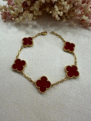 Elegant klöverarmband pläterat med 18k guld - Klöverarmband 15mm i rostfritt stål, pläterat med 18K guld 💎 I en vacker vinröd färg som ger en lyxig och sofistikerad känsla.  ✔️ Högkvalitativt rostfritt stål ✔️ 18K guldplätering ✔️ Djup vinröd färg – mycket elegant ✔️ Justerbar längd: 19 cm till första hålet, 21 cm till andra ✔️ Slitstarkt & behåller sin lyster ✔️ Väldigt fint och stilrent utförande  🌸 Perfekt för dig som älskar tidlös elegans och hög kvalitet 📩 Beställ nu och fullända din look
