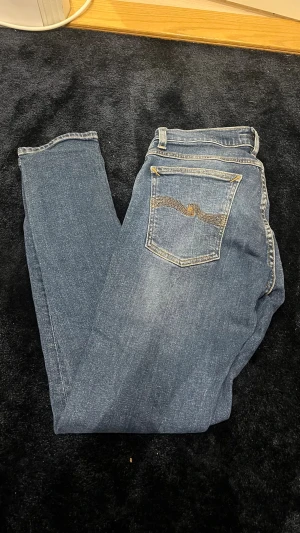 Blå nudie jeans slim fit - Säljer ett par klassiska nudie jeans med straight fit och normal passform. Jeansen har fem fickor, snygga kontrastsömmar och är tillverkade i slitstarkt bomullsjeansmaterial. Perfekta för en avslappnad och stilren look.
