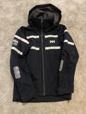 Helly hansen jacka - Säljer en helly hansen jacka storlek S som passar M. Den är vatten och vind avvisande och är perfekt till både höst och vinter. Den håller dig varm på vintern och håller dig torr till våren o hösten. Den passar verkligen allting. Jag säljer för den är inte min stil