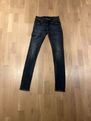 Mörkblå jeans från Tiger of Sweden - Snygga mörkblå jeans från Tiger of Sweden med klassisk femficksdesign och kontrastsömmar. Jeansen har slim passform och raka ben, med detaljer som knappstängning och läderpatch med logga bak i midjan. Perfekta för dig som gillar stilrena och tidlösa jeans.