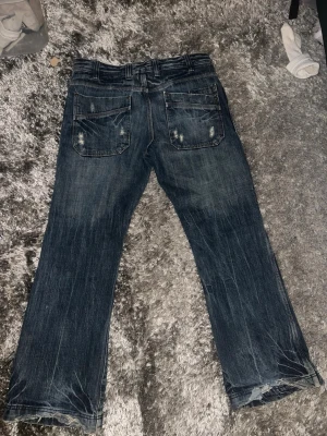 Mörkblå jeans med slitningar - Snygga mörkblå jeans med slitna detaljer och raka ben. Jeansen har klassiska bakfickor med dekorativa sömmar och en cool, lite tvättad look. Perfekta för dig som gillar en avslappnad och trendig stil.