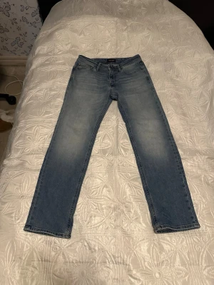Jack @ Jones - Klassiska ljusblå Jack & Jones jeans med rak passform och fem fickor. Jeansen har en snygg tvättad look med ljusare partier på låren och bakfickor med den ikoniska läderpatchen i midjan. Perfekta till vardags för en avslappnad stil. Pris går att diskutera.