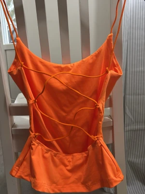 Orange topp med snörning - Snygg orange linnetopp med tunna axelband och dekorativ snörning baktill. Aldrig använd!