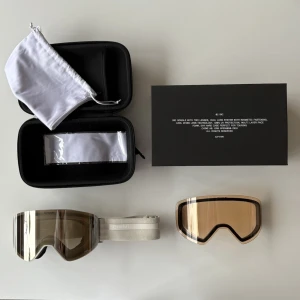 CHIMI skidglasögon med Zeiss-lins - Säljer ett par stilrena skidglasögon från CHIMI med Zeiss-lins i modell 02 sand i mycket bra skick. Glasögonen har en spegeltonad, brun lins och vitt band med CHIMI-logga. Medföljer extra lins, skyddsfodral och förvaringsväska. 