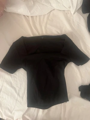 Svart offshoulder topp - Snygg svart offshoulder topp med korta ärmar och figurnära passform. Perfekt att styla med jeans eller kjol för en trendig look. Enkel och stilren design utan synliga detaljer eller mönster.