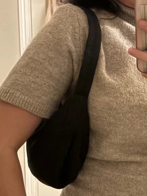 Svart och beige axelväska - Två stilrena axelväskor i svart och beige med mjuk, vadderad känsla. Väskorna har en enkel, rundad form och bred axelrem som gör dem bekväma att bära. Perfekta för att slänga över axeln till vardagslooken. Materialet är slätt och lätt att torka av.