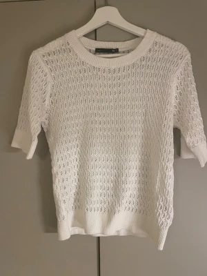 Vit stickad topp från 157, S - Säljer en vit stickad topp från 157 i storlek S. Tröjan har korta ärmar och ett genombrutet, hålmönstrat stickat material som ger en luftig känsla. Rund halsringning och ribbade muddar vid ärmslut och nederkant. Perfekt för vår och sommar!