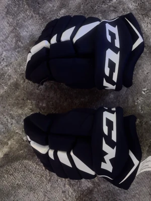 CCM FT475 hockeyhandskar 12 tum - Säljer ett par mörkblå CCM FT475 hockeyhandskar med vita detaljer och logga. Insidan är ljusbeige med svarta förstärkningar vid fingrarna. Handskarna har en sportig look och är designade för hockeyspelare som vill ha bra skydd och komfort.