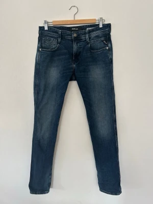 Replay Anbass Slim Fit Jeans Blå 30 - Säljer ett par Replay Anbass slim fit jeans i mörkblå tvätt med snygga slitningar. Klassisk femficksmodell med dragkedjegylf och Replay-logga på fickan. Jeansen är tillverkade i stretchig bomullsdenim för skön passform.