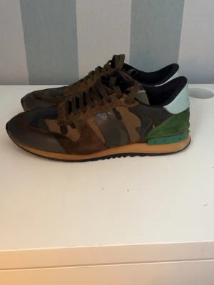 Valentino Rockrunner sneakers camouflage - Säljer ett par Valentino Rockrunner sneakers med camomönster i brunt, grönt och svart. Skorna har detaljer i mocka, skinn och textil samt coola nitar på hälen. Snygg kontrast med grön och ljusblå bakkappa. Skorna är storlek 44 men passar 45, och priset kan diskuteras vid snabba affär 
