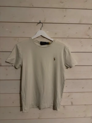 Beige t-shirt från Polo Ralph Lauren - Snygg beige t-shirt från Polo Ralph Lauren i custom slim fit. Klassisk design med korta ärmar och den ikoniska broderade loggan på bröstet. Tillverkad i mjuk bomull som känns skön mot huden. Perfekt till jeans eller shorts för en clean look. Sitter typ som 170, gör en bundle för ett schysst pris 