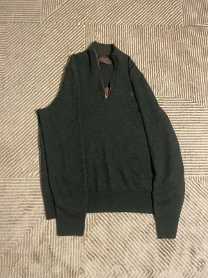 Mörkgrå stickad tröja Morris - Mörkgrå stickad tröja från Morris med halv dragkedja och liten broderad logga på bröstet. Tröjan har lång ärm, ribbade muddar och klassisk passform. Perfekt till jeans för en clean look. St 152