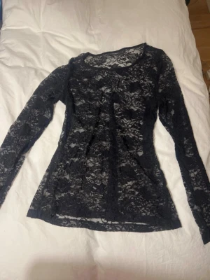Svart spetsblus från Lindex - Säljer en svart långärmad spetsblus från Lindex i storlek L. Blusen är helt genombruten med ett blommigt spetsmönster och har en rund halsringning. Perfekt att styla lager på lager eller med ett linne under.