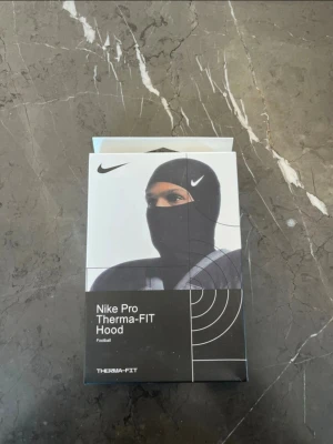 Nike Pro Therma-FIT Hood - Nike Pro Therma-FIT Hood är en svart huva designad för fotboll. Den är tillverkad i ett värmande och stretchigt material som håller dig varm under kalla träningspass. Perfekt för att bära under hjälm eller mössa.